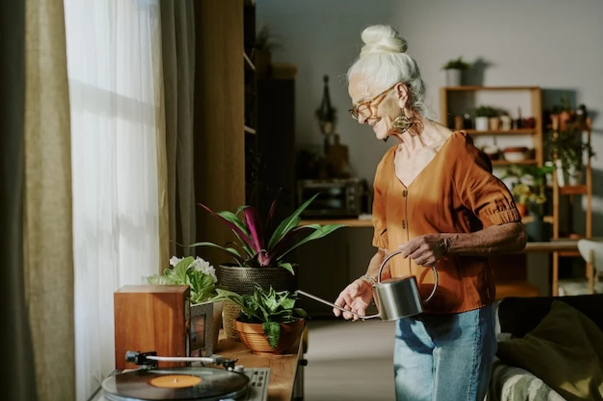 happy senior watering indoor plants during daylight window
